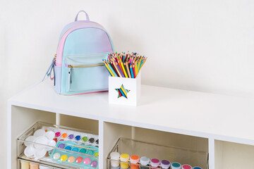 White shelving with kids backpack and various material for creativity and art activity. Stationery and supplies for drawing and craft. Organizing and storage in childrens room.