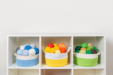 Storage baskets with colored balls of yarn for knitting. Bright yarn balls on the shelves. Organizing and storage in craft room. Handmade, needle craft, creativity and  hobby.