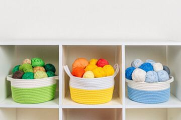 Storage baskets with colored balls of yarn for knitting. Bright yarn balls on the shelves....