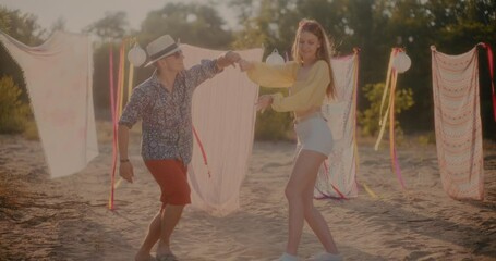 Young couple dancing against sarongs hanging at beach - Powered by Adobe