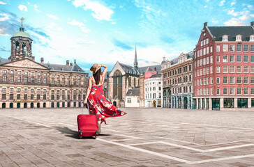 Obraz premium Amsterdam Netherlands - Traveler woman in red dress and suitcase, walks on Dam square, Amsterdam on summer vacation in Holland - Europe summer travel concept.