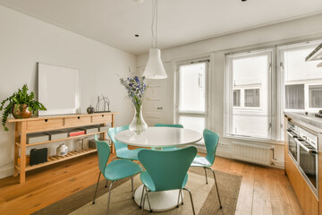 a dining room with white walls and wood flooring the table is surrounded by four blue chairs in front of the window