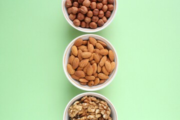 Assortment of nuts in ceramic bowls. Walnut, hazelnut, almond on green background. Organic raw food mix. Top view, copy space