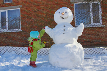 a child is playing with a snowman,Happy child girl playing with a snowman on a winter walk