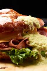 Little croissant with ham, bacon, yellow cheese and orejona lettuce, still sided with a roll of ham, bacon and lettuce, placed on a wooden base.