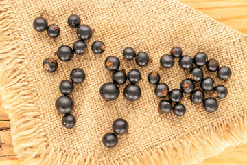 Several organic blackcurrant berries with  jute napkin on wooden table, macro, top view.