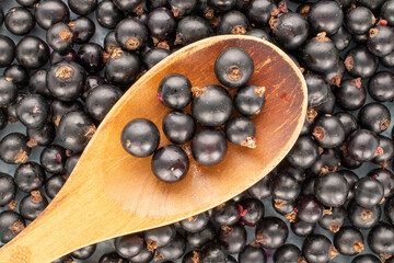 Several sweet blackcurrant berries with wooden spoon, macro, top view.