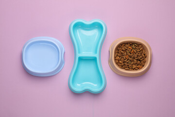Different shapes and colors of animal feeding bowls, with dry food and water, in the shape of a bone on pink background. Top view