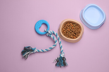 Pet toy and a bowl of dry food and water on a pink background. Top view