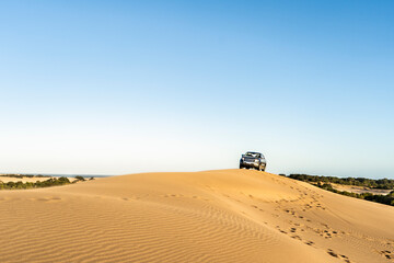 Fototapeta na wymiar A man driving a 4x4 vehicle in a dune at sunset