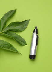 Electric shaver for the nose on a green background with leaves. Top view