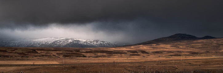 Panorama of a mountain range covered with snow clouds and a road in the valley. Cairngorms National Park, Highlands, Scotland