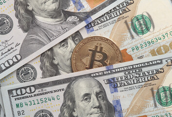 Bitcoin among hundred dollar bills close up