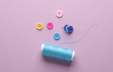Fototapeta na wymiar Skein of blue thread and a needle, buttons on lavender color background. Sewing accessories