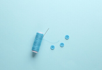 Skein of blue thread and a needle, buttons on blue background. Sewing accessories