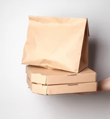 Gordijnen Takeaway food. Zero waste. Hand holding Craft cardboard pizza boxes and paper bag on gray background. Eco concept. © splitov27