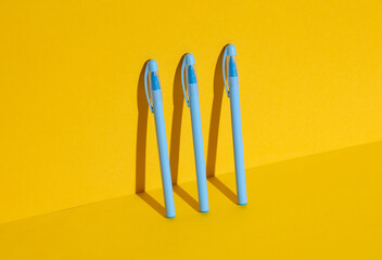 Plastic blue pens on yellow background. Business, education concept. Creative layout, minimalism. Modern art