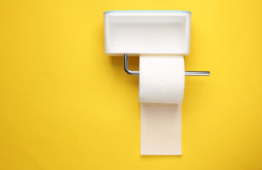 Toilet paper holder with a roll of toilet paper on a yellow wall. minimalistic photo