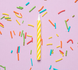 Yellow birthday candle with  sprinkles on pastel background. Minimalism party concept