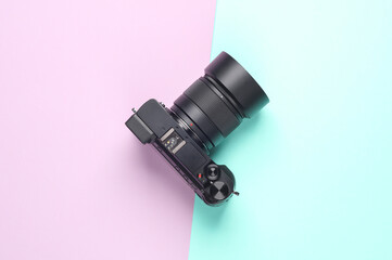 Modern digital mirrorless camera with a lens on a blue-pink pastel background. Top view. Minimalism
