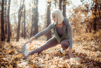 Active and energetic fit blond woman practicing leg stretching in autumn forest