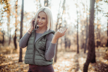 Smiling fitness blonde woman talking on the phone in autumn forest