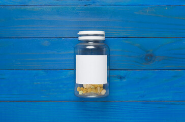 Plastic bottle with vitamins on wooden background, top view