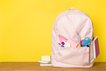 Pink school backpack with stationery on wooden table