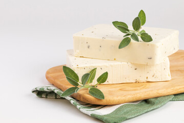 Two pieces of tofu, paneer or soy cheese with fresh sage leaves on wooden cutting Board with green...
