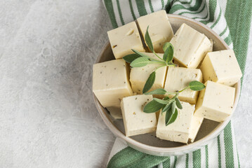 Tofu soy cheese or paneer or feta cheese cubes adding fresh sage in a ceramic bowl on a striped...