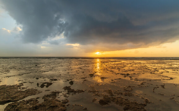 beautiful sunrise at a mirrored beach with a cloudy sky. The sun are reflected on the water in a strong yellow
