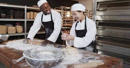 Happy diverse bakers working in bakery kitchen, rolling dough on counter in slow motion