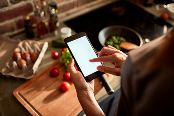 Young woman using a smart phone while cooking in the kitchen