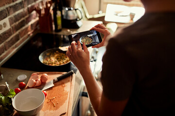 Young woman using a smart phone to take a picture of a meal she is cooking