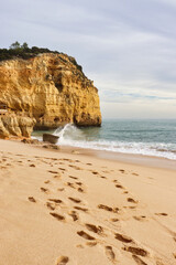 Footprints in sand on beach with water splashing on rock on a winter day in southern Portugal on the Seven Hanging Valleys Trail.