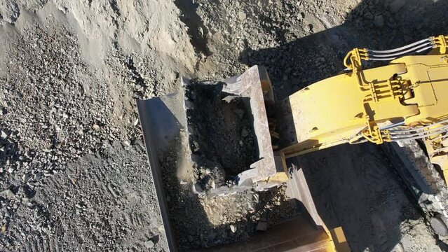 Large bucket excavator loads ore into a large dump truck in open mine gold digging pit, slow motion aerial shot