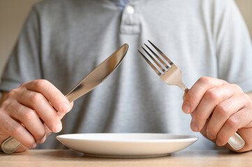 Waiting for food: empty white plate, male hands holding fork and knife - obrazy, fototapety, plakaty