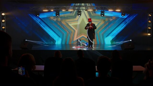 Creepy clown mime showing magic tricks on stage during talent show audition. Swallowing the air balloon. Broadcast television style TV entertainment program 