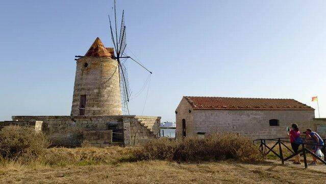 Slow motion of tourists taking picture of Mulino Maria Stella windmill in front of saline in province of Trapani, Sicily. Italy