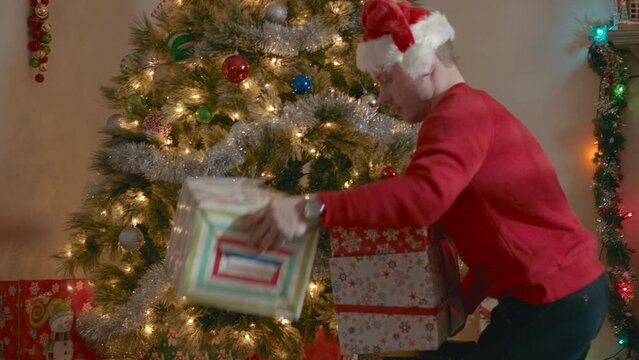 College student in red Santa hat stacks presents under Christmas tree