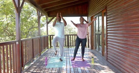 Happy senior african american couple practicing yoga on mats on sunny terrace, slow motion