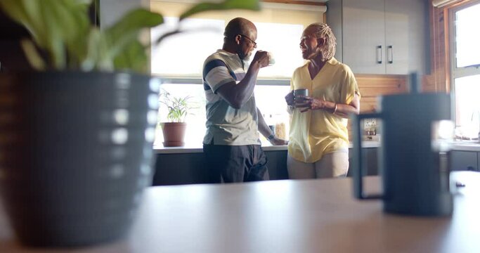 Happy senior african american couple drinking coffee and talking in kitchen, slow motion