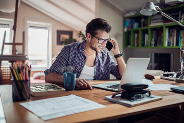 Young man using a laptop at home while talking on the phone