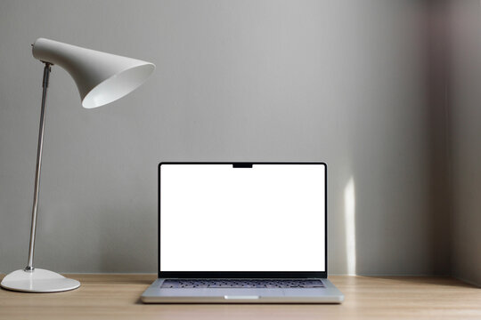laptop with white screen on a wooden table. Gray background. White lamp on the table.laptop on the table with space for a signature. Macbook 14 pro 2021. gray wall, hotel workplace.copy space