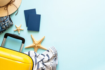 Travel background, summer holidays. Suitcase, passports, hat and summer cloth on blue background. Flat lay image with copy space.