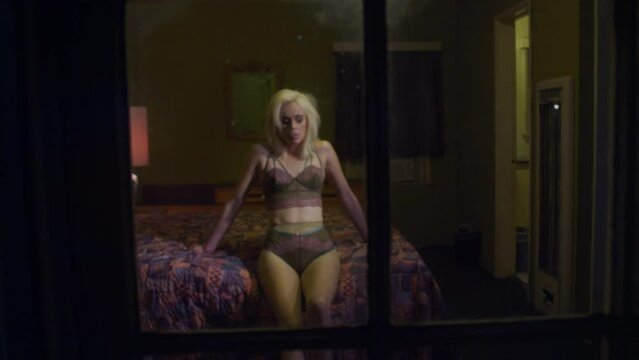 Dark portrait of a woman in lingerie smoking a vaporizer on a motel bed