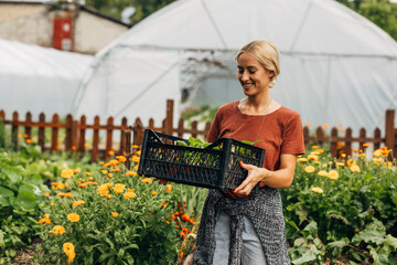 Joyful woman in the garden carrying crate with plants.