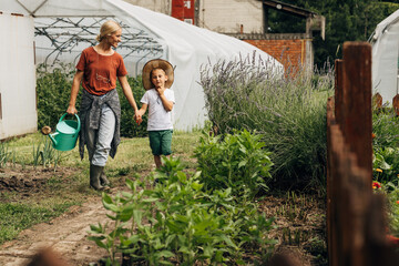 Mother is holding er sons hand while they walk trough their garden.