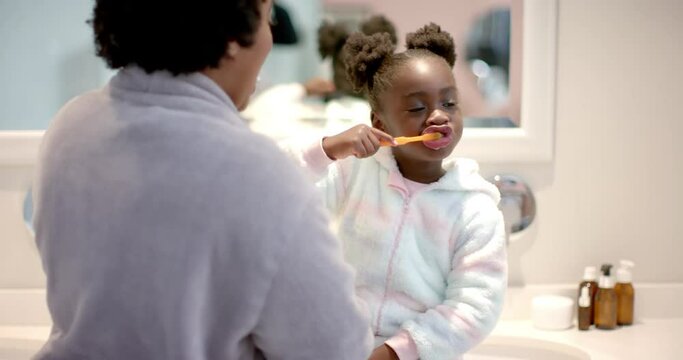 Happy african american mother and daughter brushing teeth in bathroom, slow motion