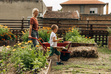 Side view of mother and son walking trough the garden with a cart